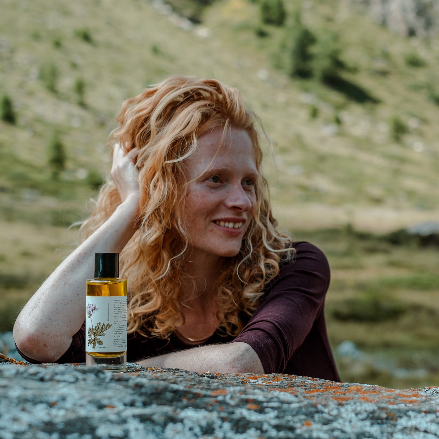 Eine Frau mit roten locken posiert in der Natur, vor ihr steht das regenerierende Körperöl von Botanik Atelier. 