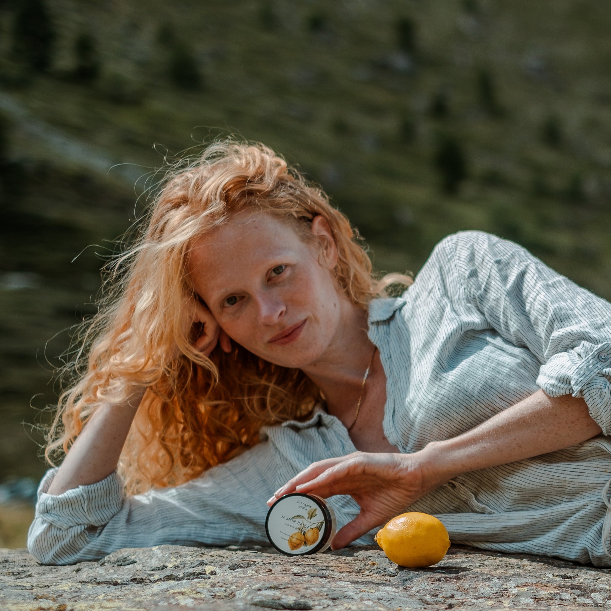 Junge Frau mit roten Haaren posiert in der Natur mit dem Jasmin Balsam von Botanik Atelier und einer gelben Zitrone. 