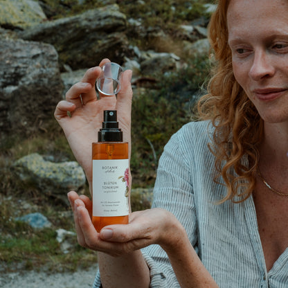 Frau mit roten Locken öffnet das ausgleichende Blüten Tonikum mit 5% Niacinamide von Botanik Atelier.